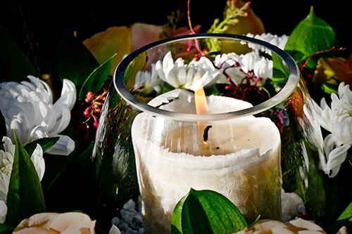 Una vela blanca está rodeada de flores y hojas blancas.