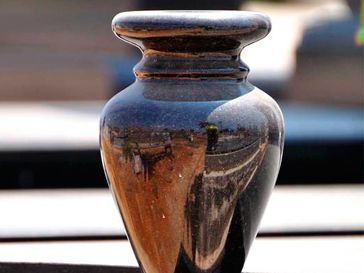 Un pequeño jarrón negro está sobre una mesa.