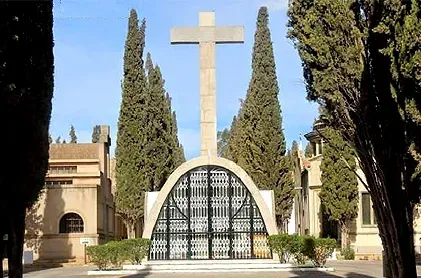 Una gran cruz está en medio de un cementerio rodeado de árboles.