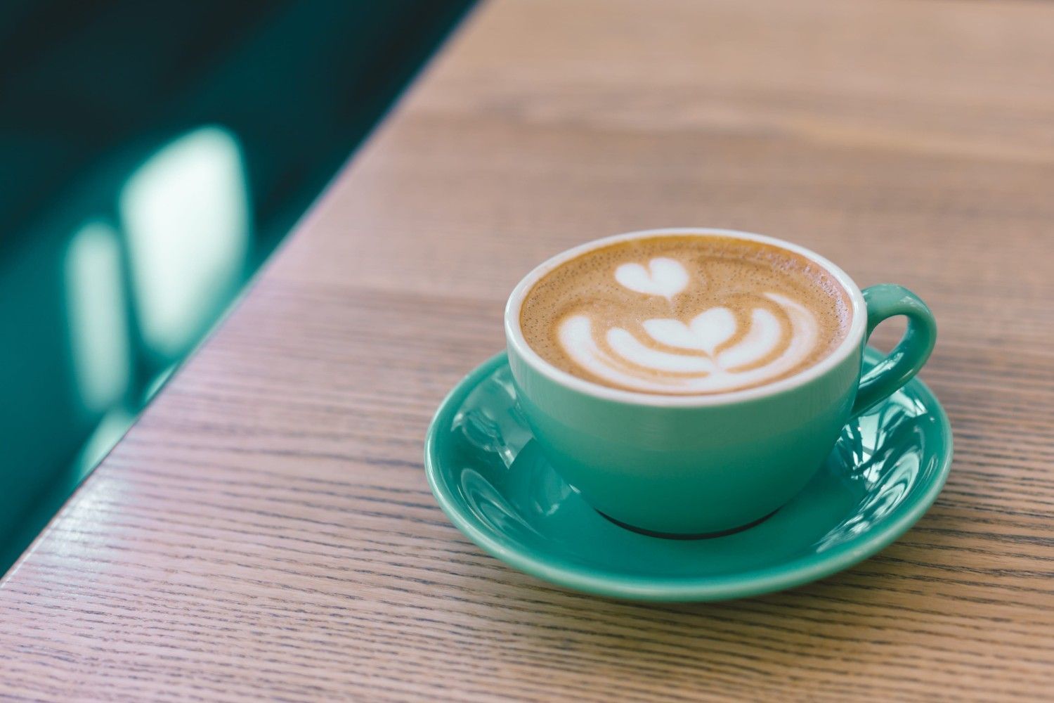 Una taza de café de cerámica color turquesa con un dibujo de latte art en forma de corazón.
