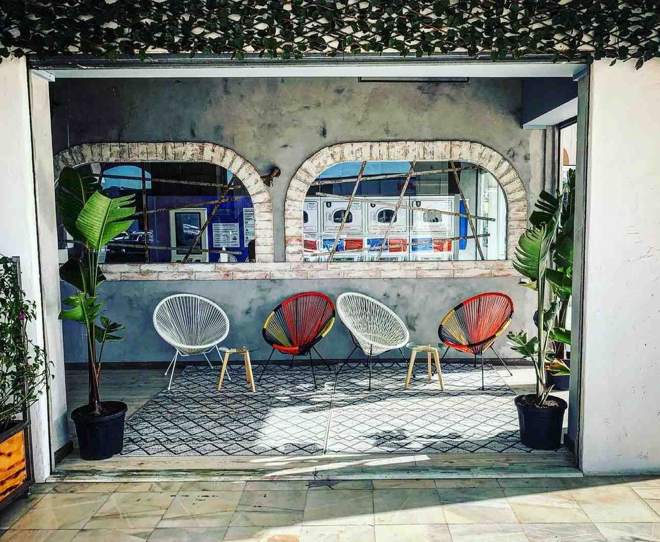 Una zona de estar con cuatro sillas de mimbre y dos mesitas sobre una alfombra estampada, enmarcada.