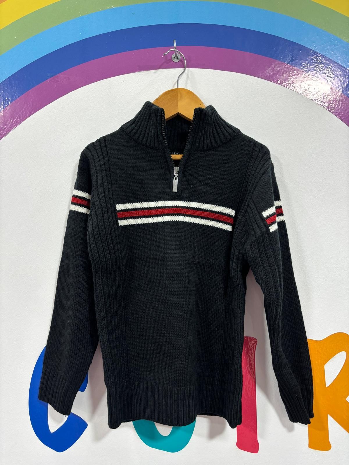 Un suéter negro con rayas rojas, blancas y azules está colgado en una percha.