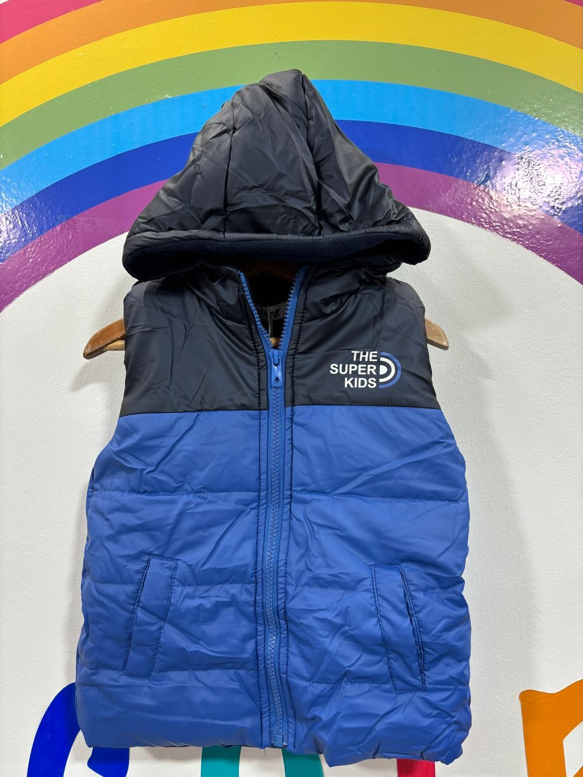 Un chaleco azul y negro con capucha está colgado en una percha.