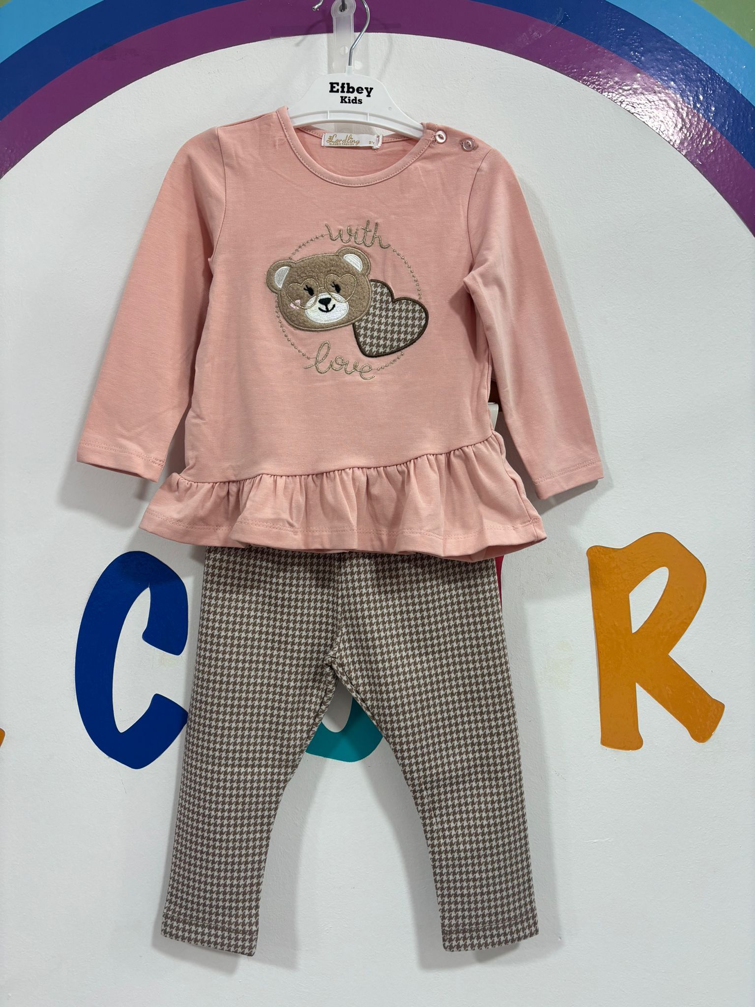 Una camisa rosa con un osito de peluche está colgada en una percha.