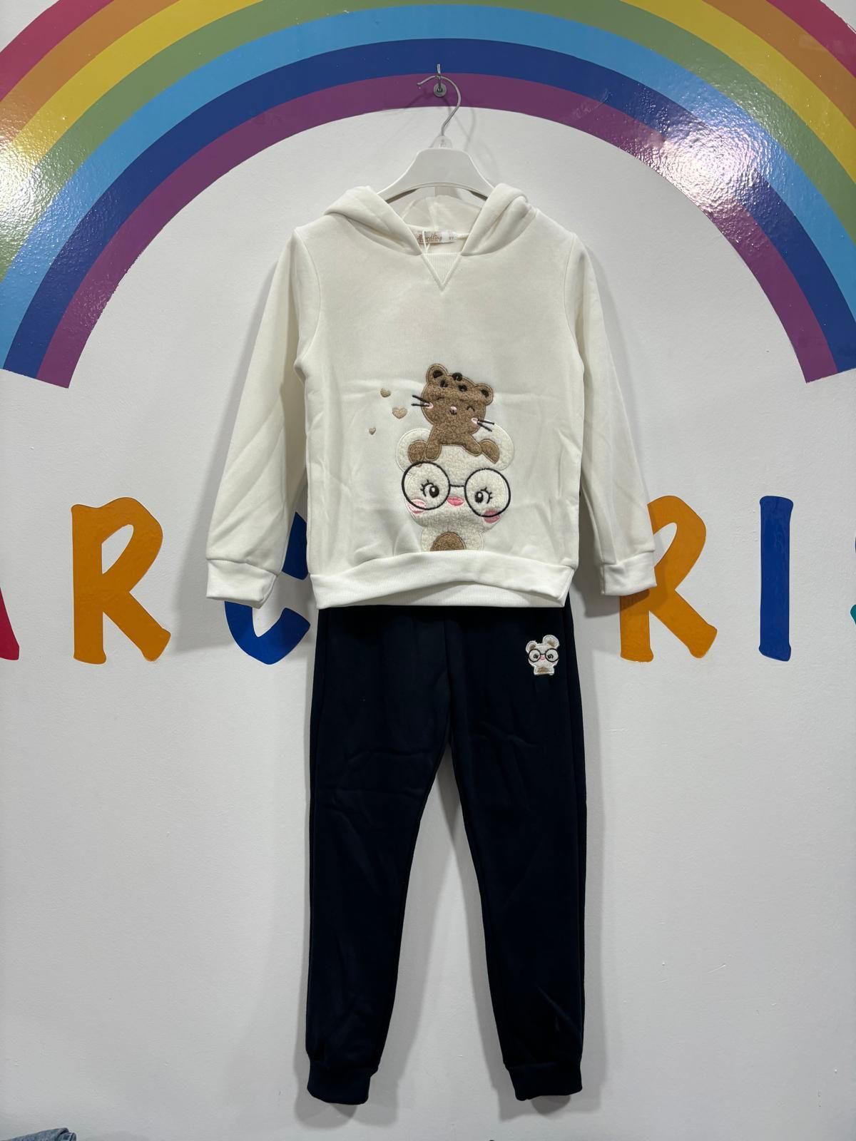 Una sudadera con capucha blanca con un osito de peluche está colgada en una percha frente a un arcoíris.