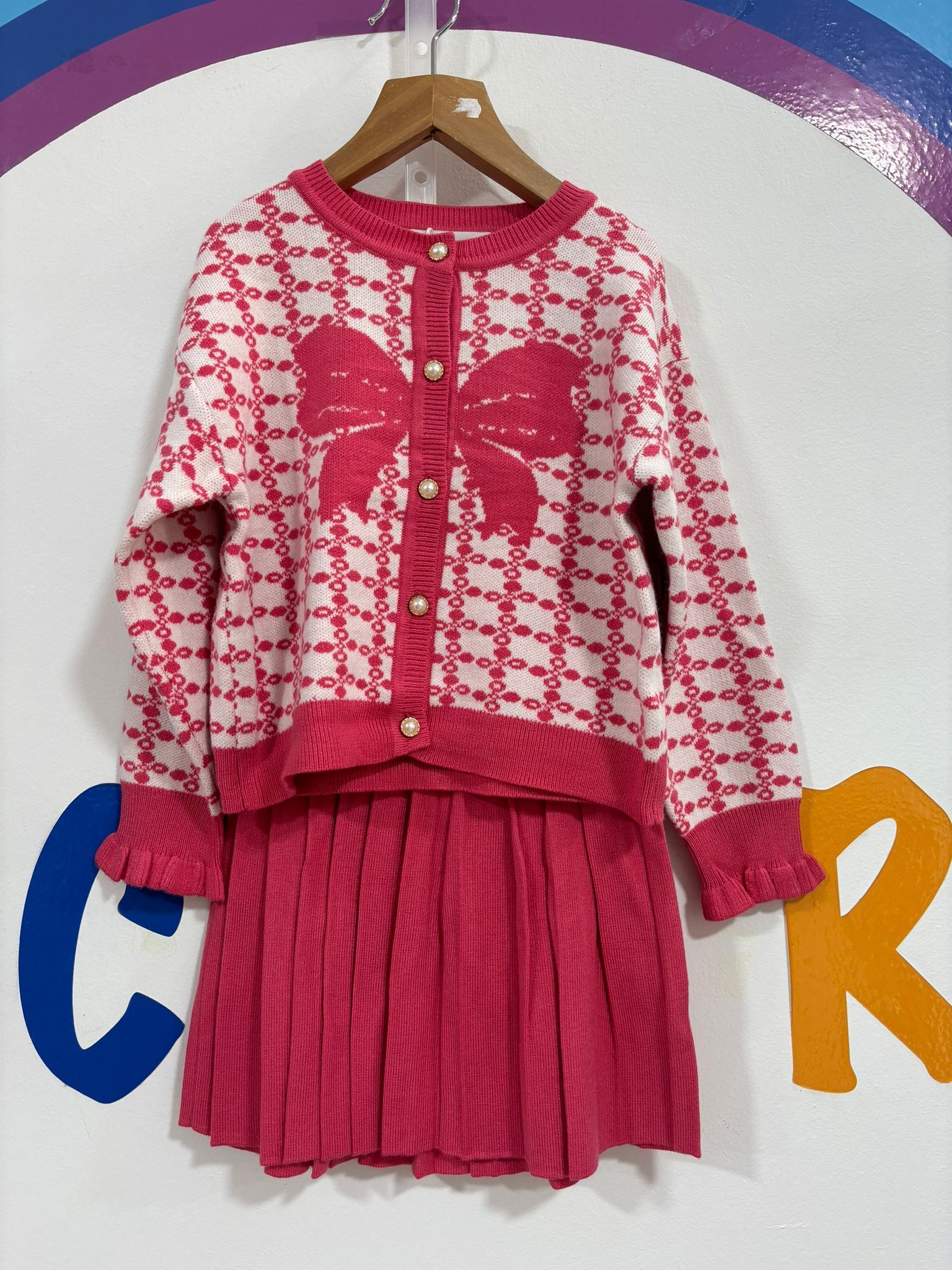 Un suéter rosa y blanco con una mariposa está colgado en una percha.