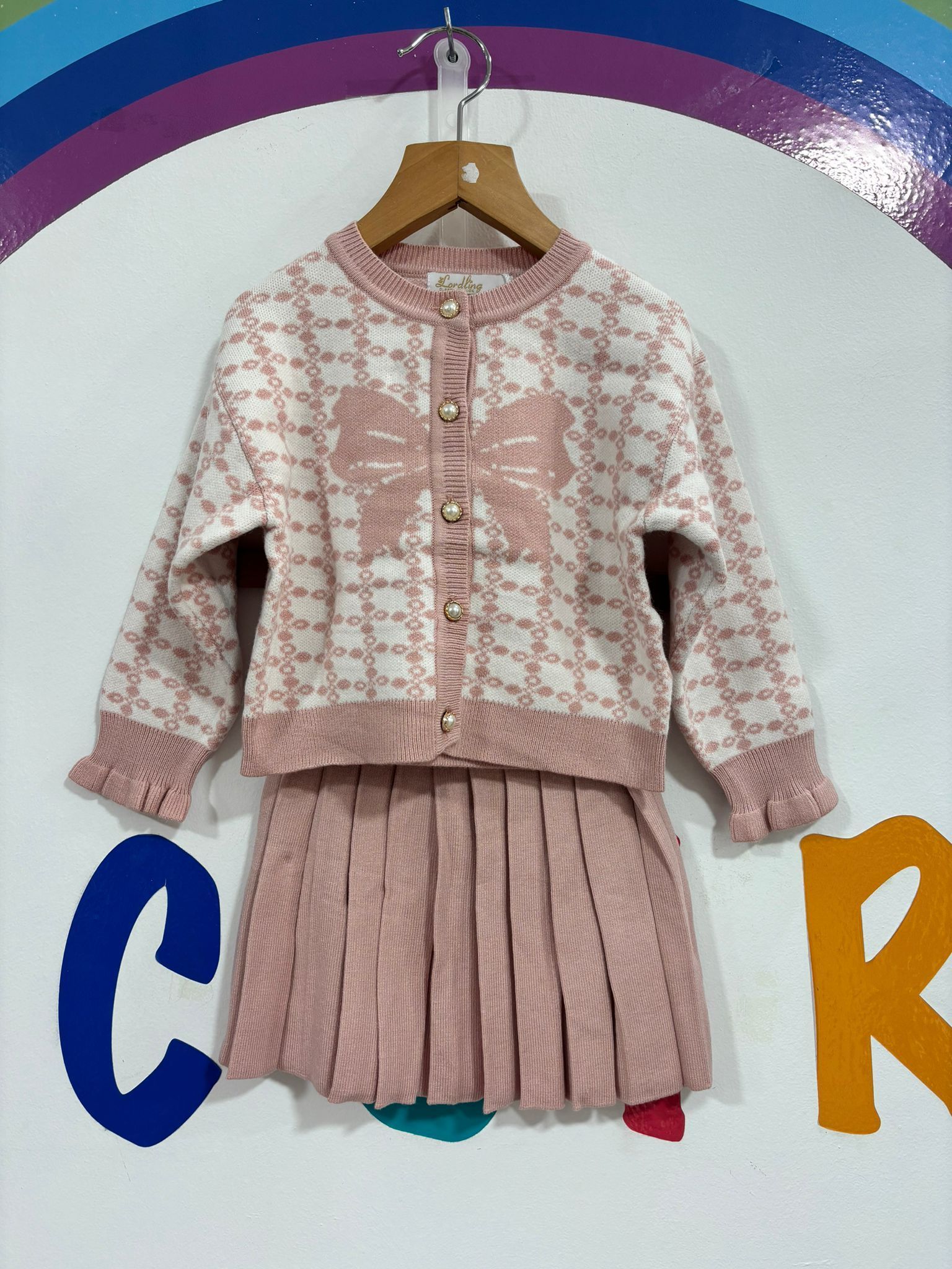 Un conjunto de suéter y falda rosa y blanco colgado en una percha.