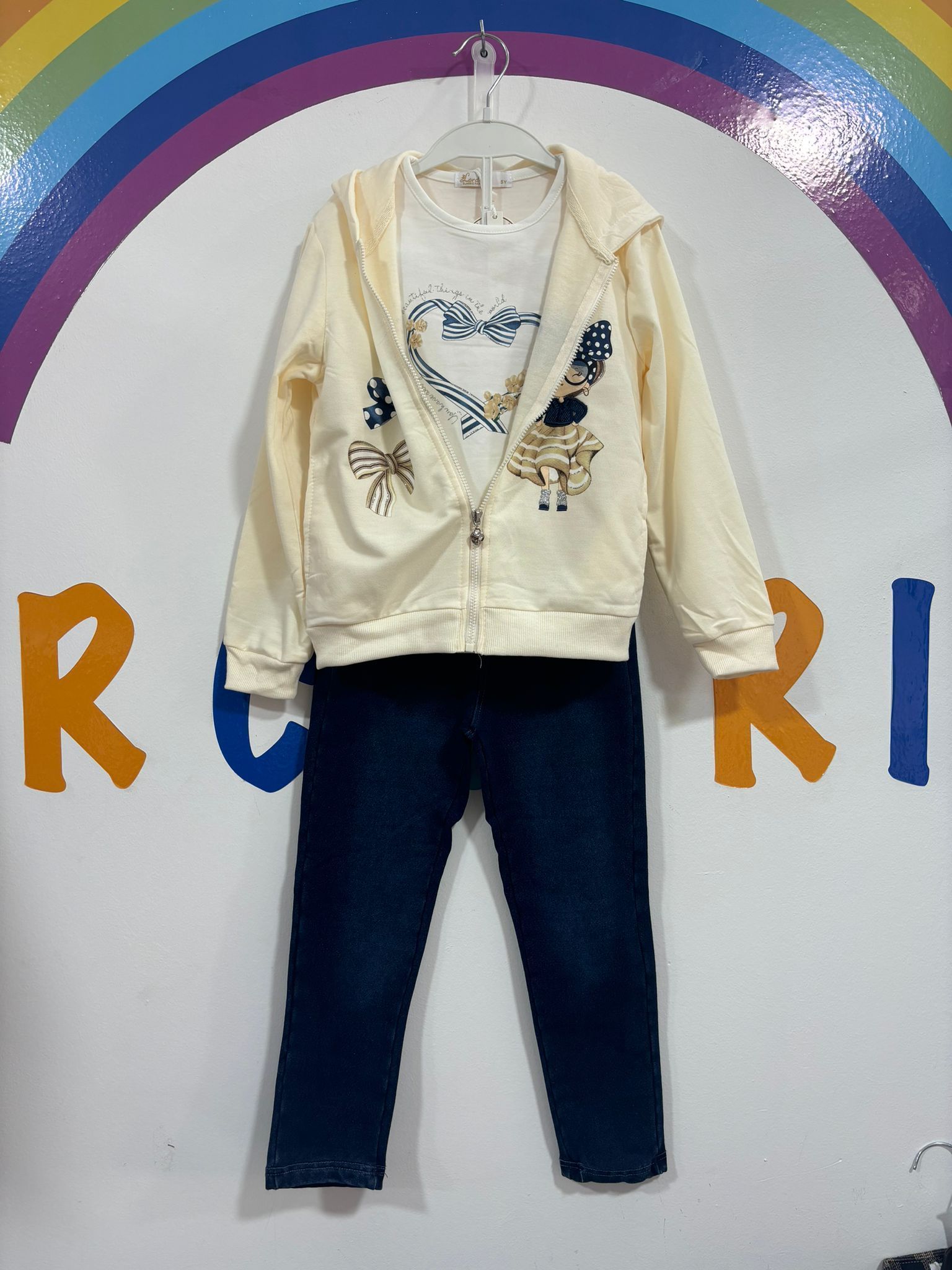 El atuendo de un niño está colgado en una percha frente a un arcoíris.