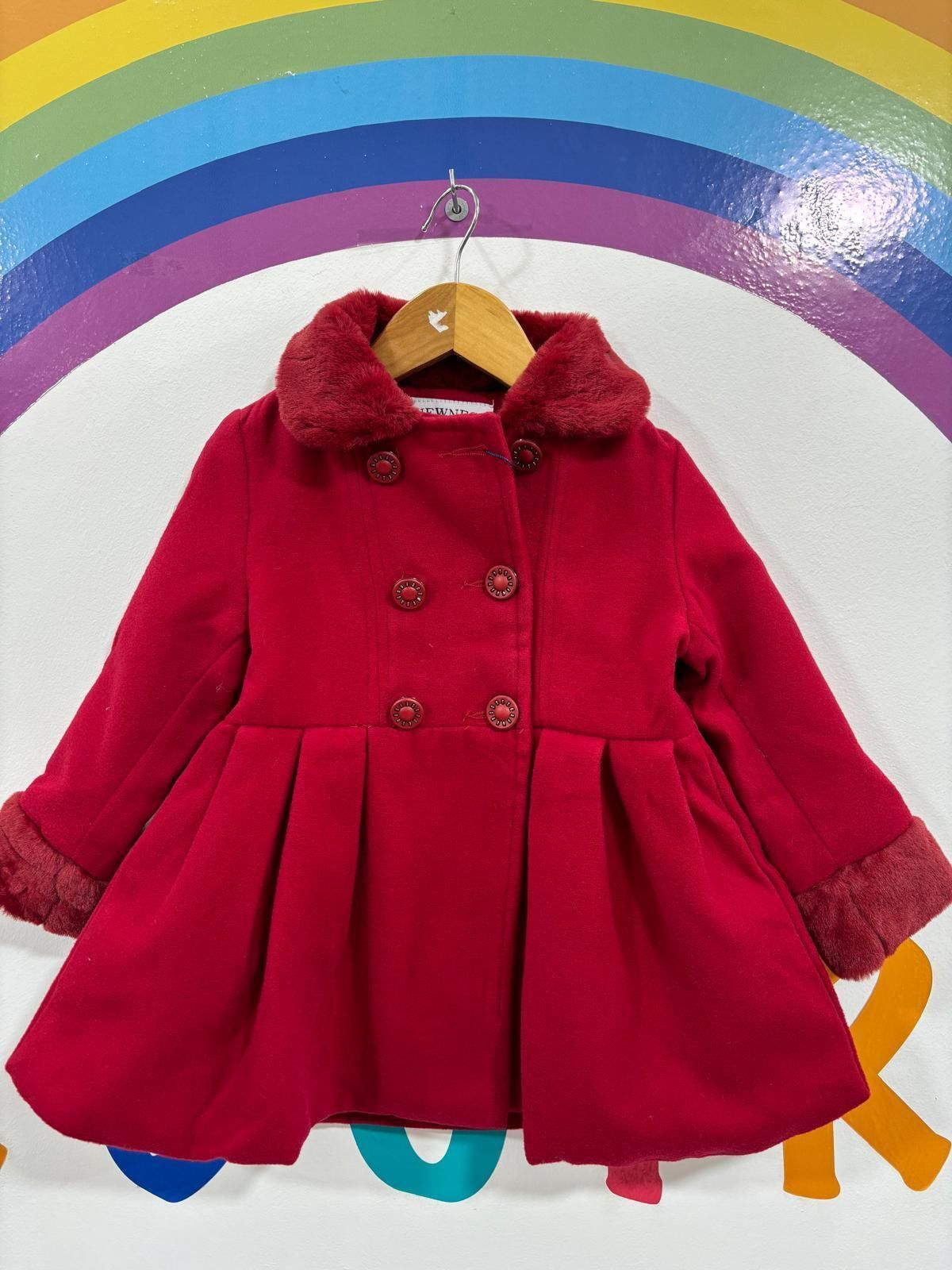 Un abrigo rojo está colgado en una percha delante de un arcoíris.