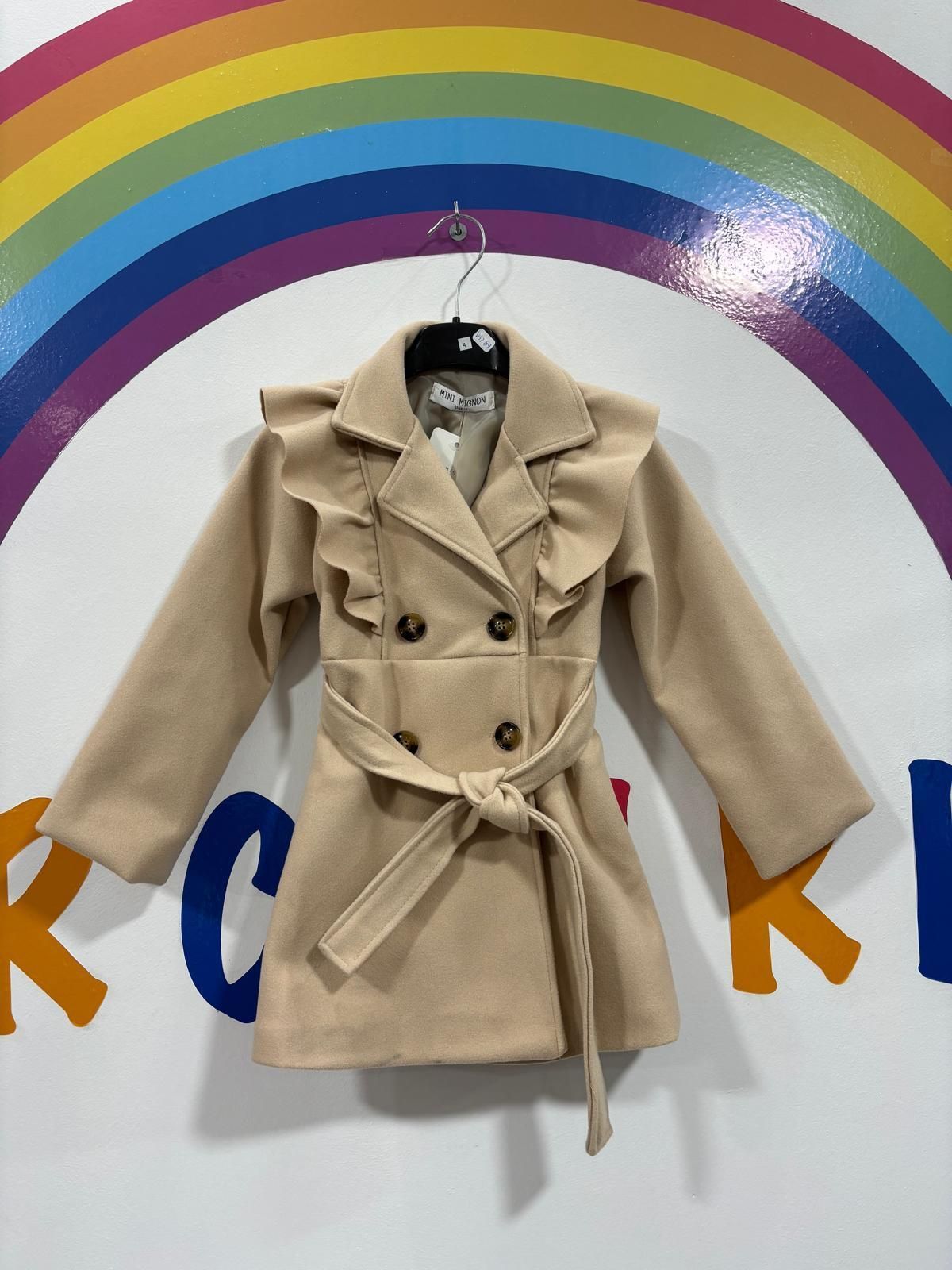 Un abrigo beige con volantes cuelga de una percha delante de un arcoíris.