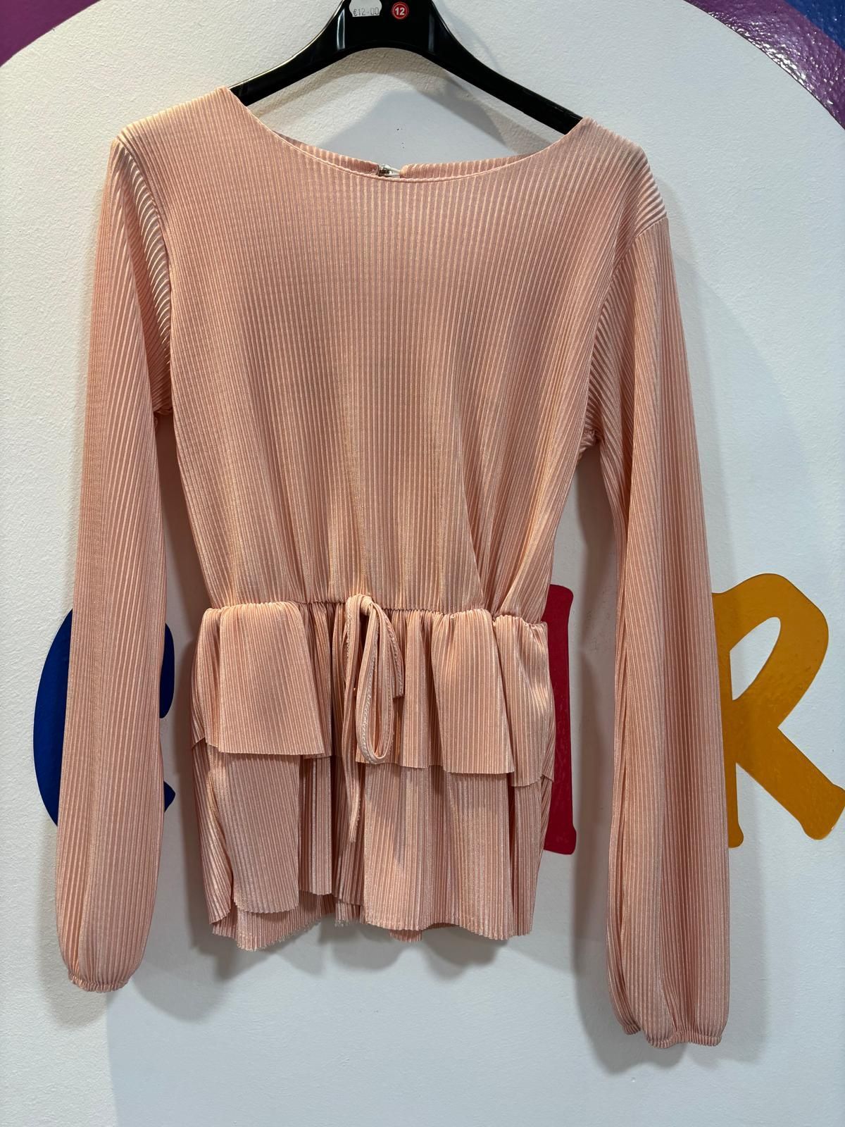 Una blusa rosa con mangas largas está colgada en una percha.