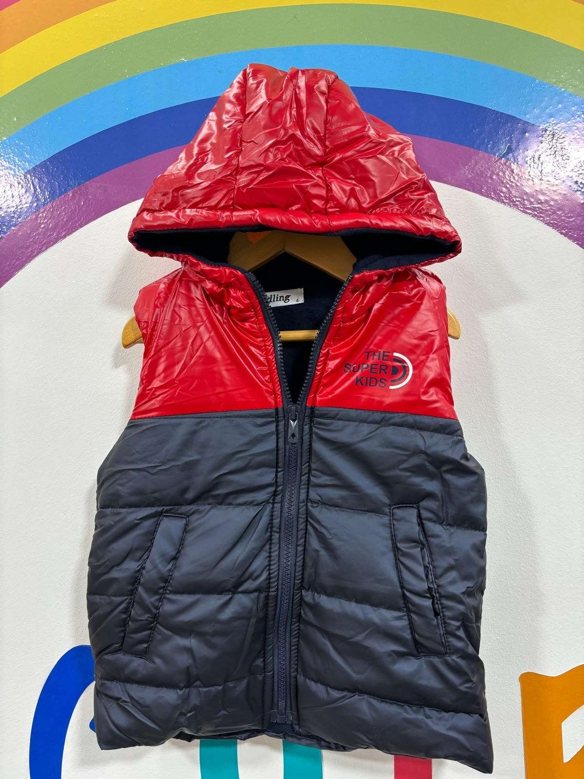 Un chaleco rojo y negro con capucha está colgado en una percha.