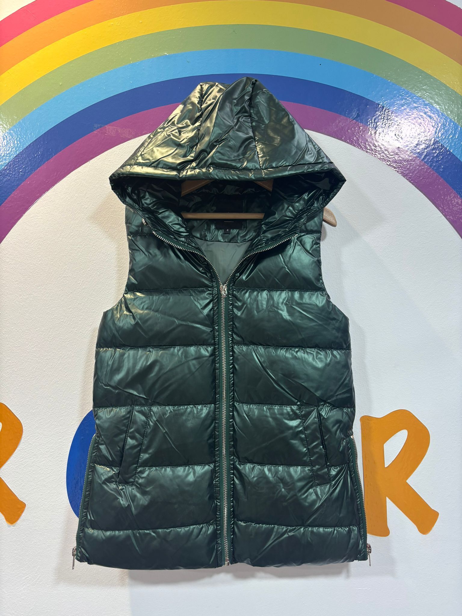 Un chaleco verde con capucha cuelga de una percha delante de un arco iris.