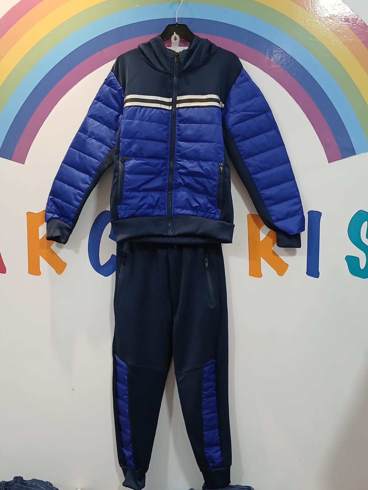 Una chaqueta y unos pantalones azules cuelgan de una percha delante de un arcoíris.