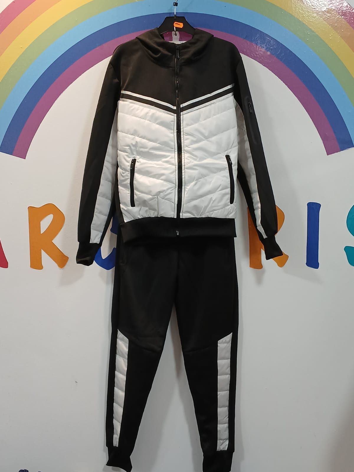 Un chándal blanco y negro cuelga en una percha delante de un arcoíris.