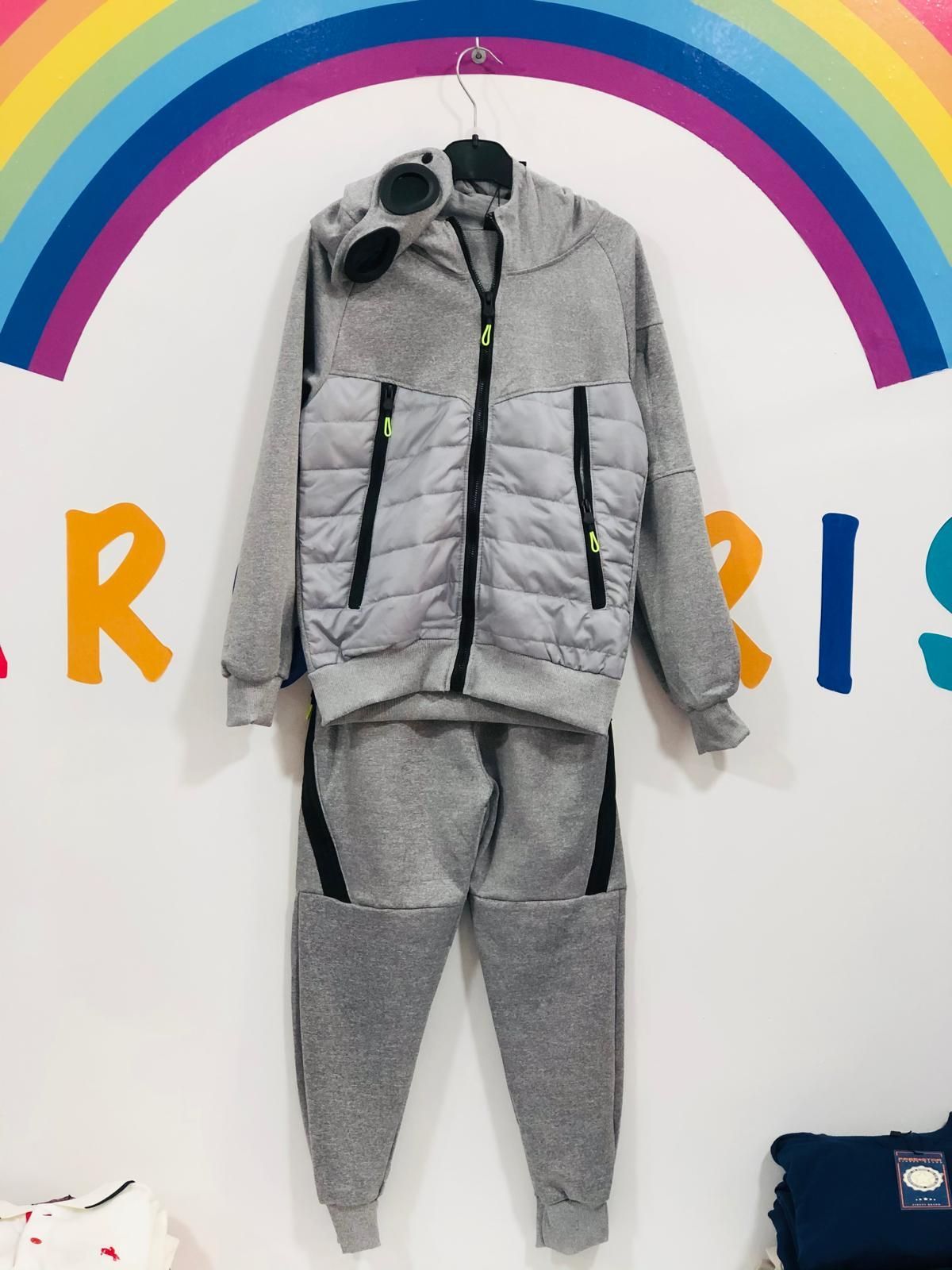 Una chaqueta y unos pantalones grises cuelgan de una percha con un arcoíris de fondo.