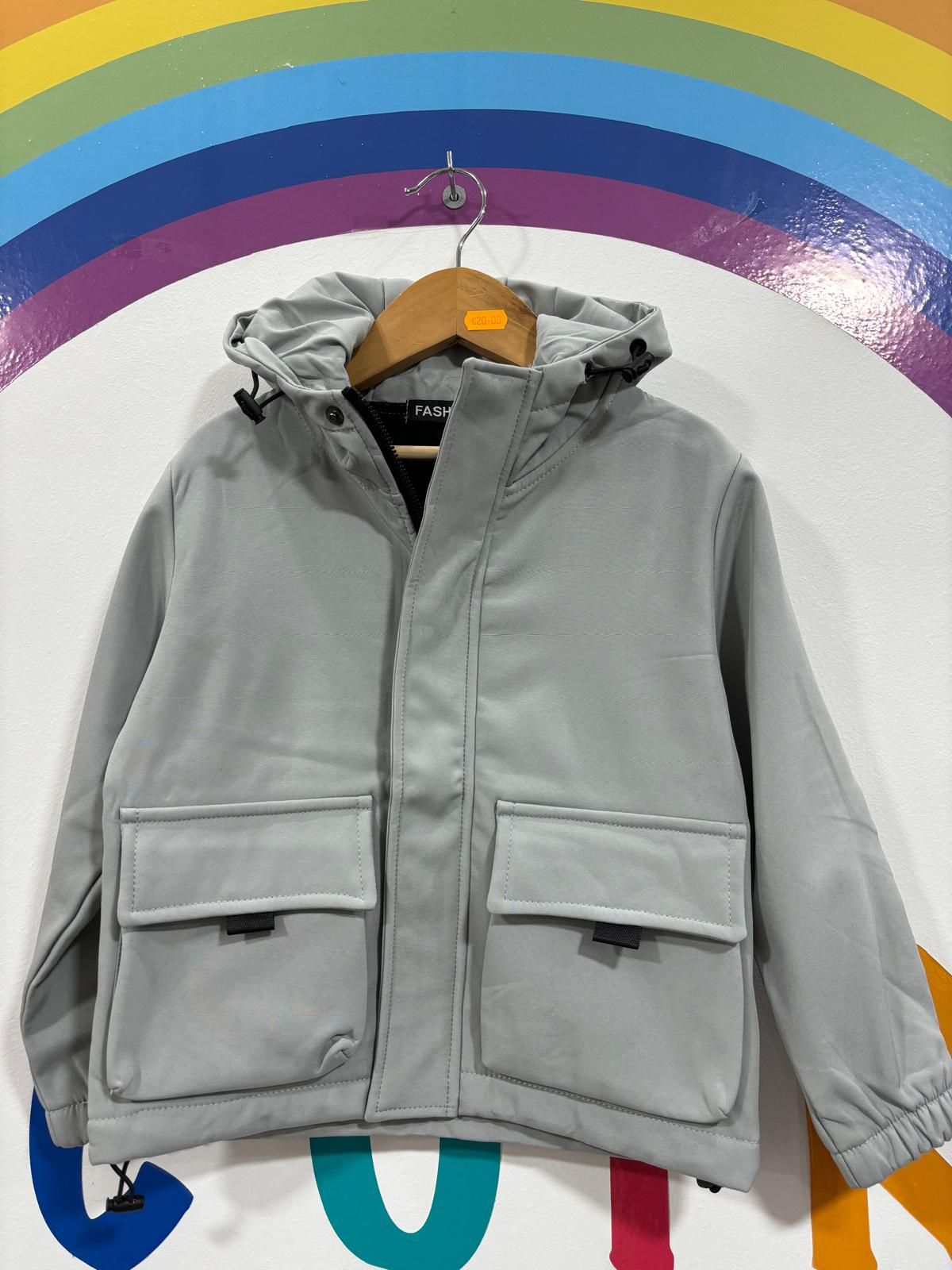 Una chaqueta gris con capucha cuelga de una percha delante de un arcoíris.