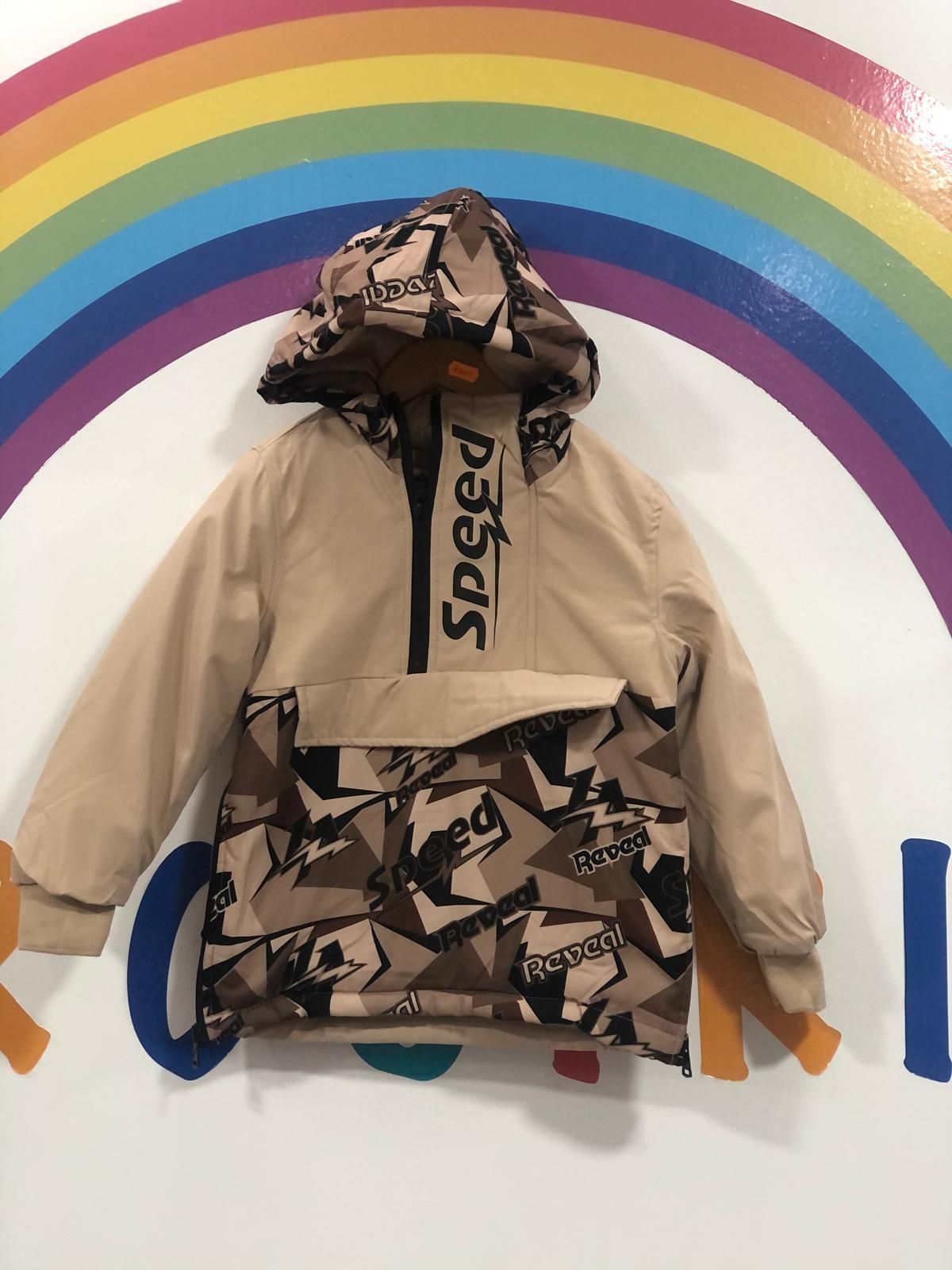 Una chaqueta con capucha está colgada en una pared al lado de un arco iris.