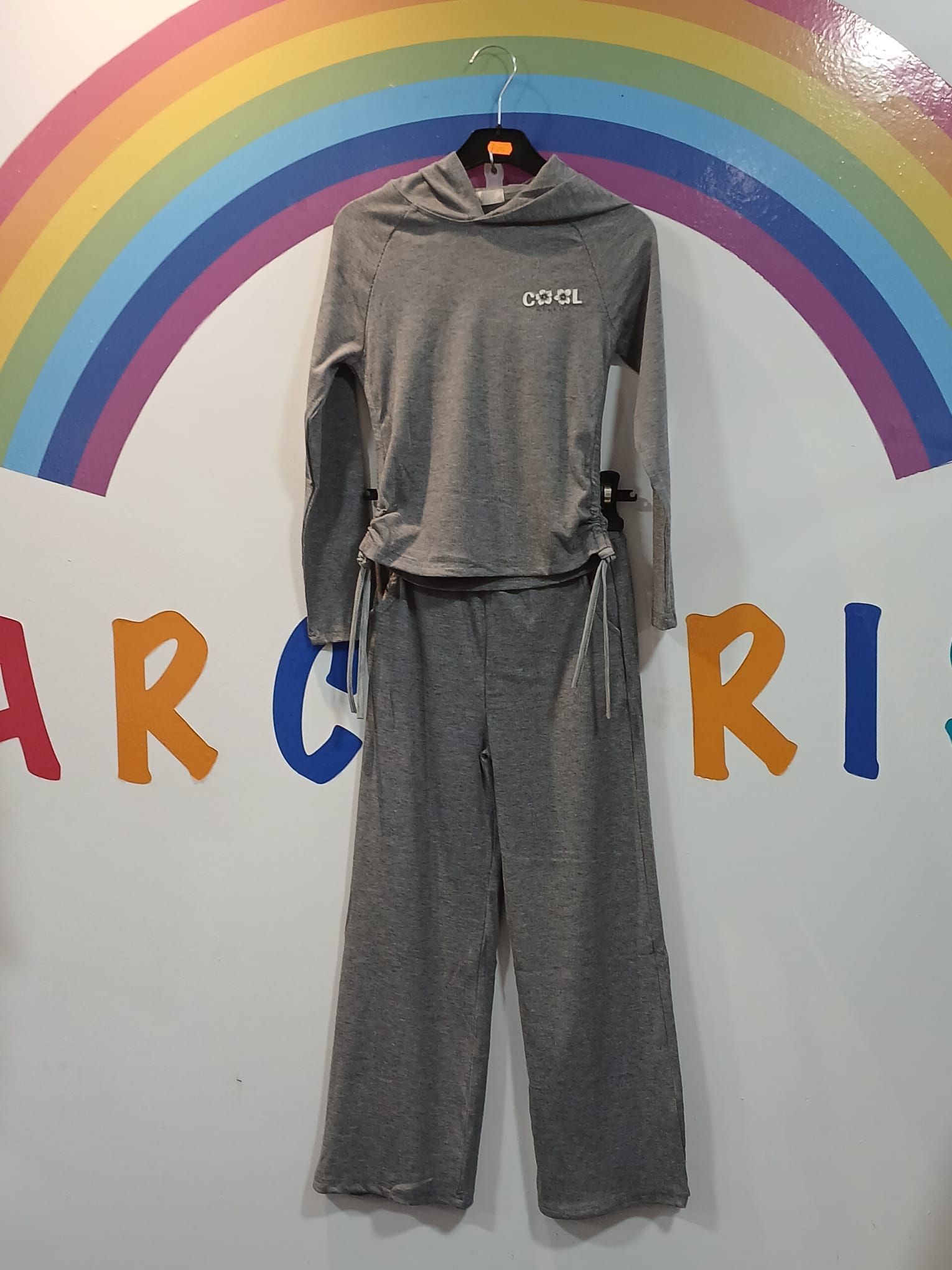 Una sudadera con capucha gris y unos pantalones cuelgan de una percha delante de un arcoíris.