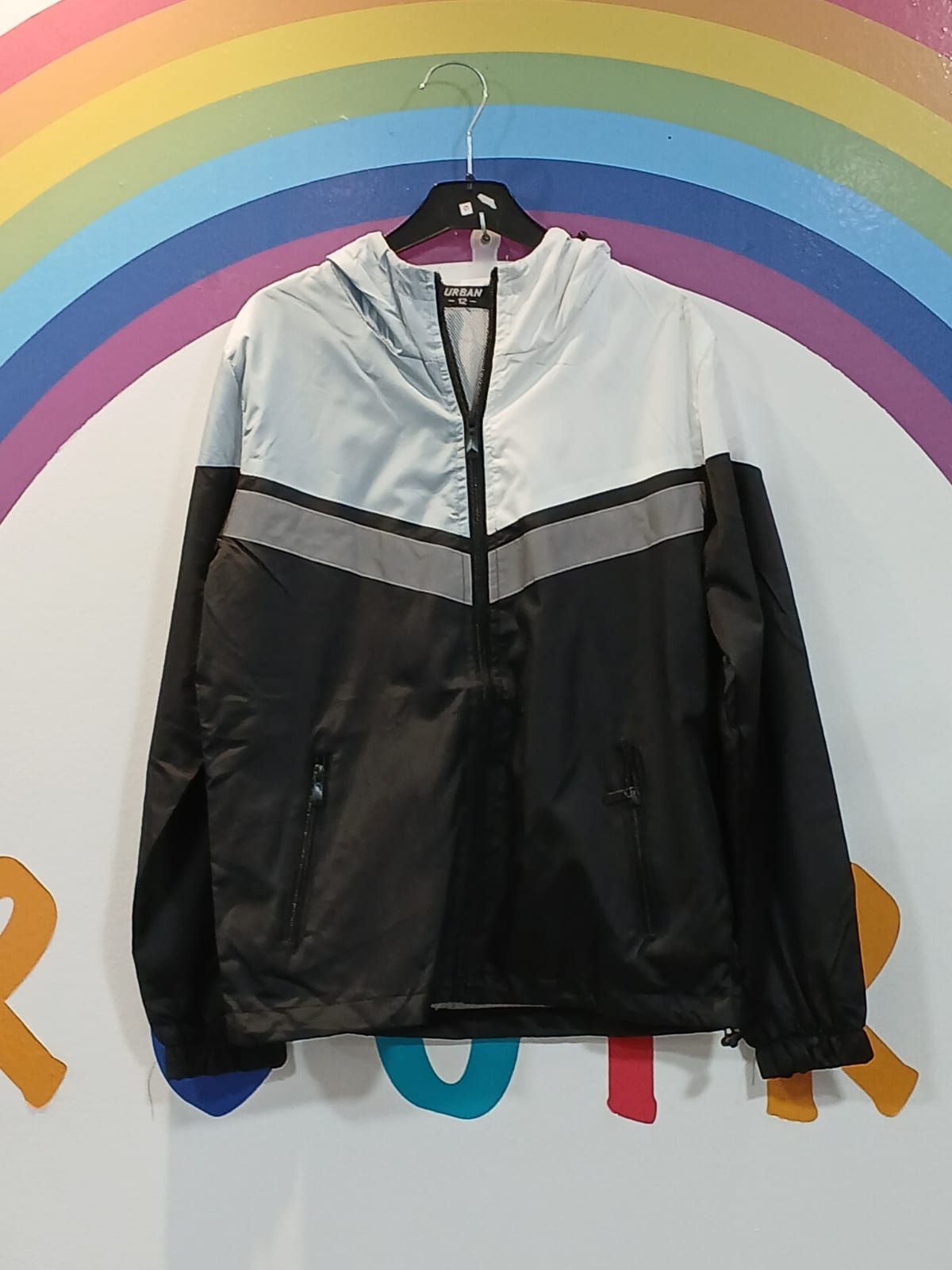 Una chaqueta blanca y negra cuelga en una percha delante de un arcoíris.