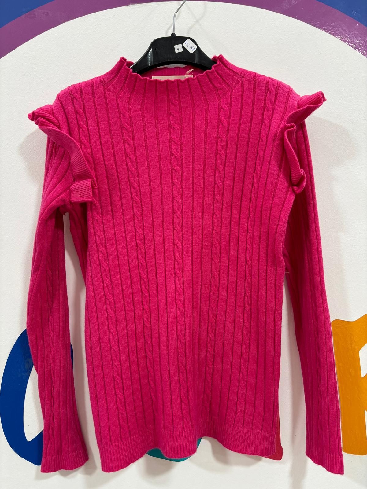 Un suéter rosa con mangas con volantes cuelga de una percha.