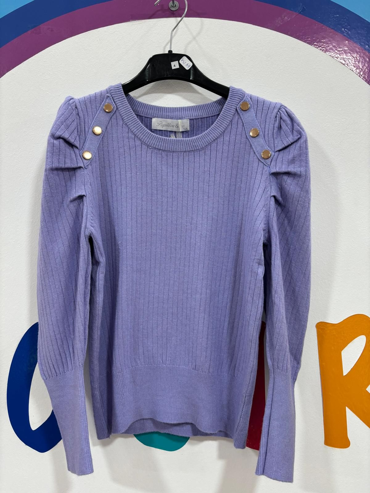 Un suéter morado con botones dorados en los hombros está colgado en una percha.