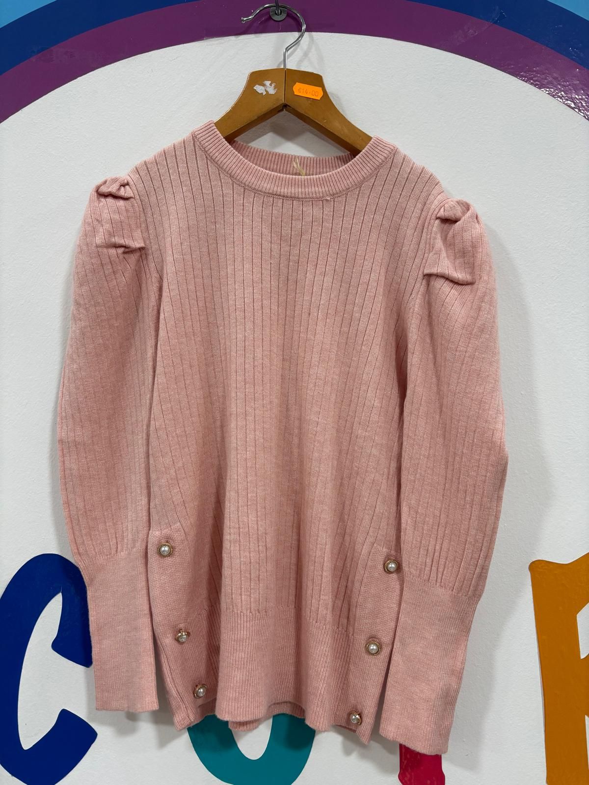 Un suéter rosa con botones en las mangas está colgado en una percha.