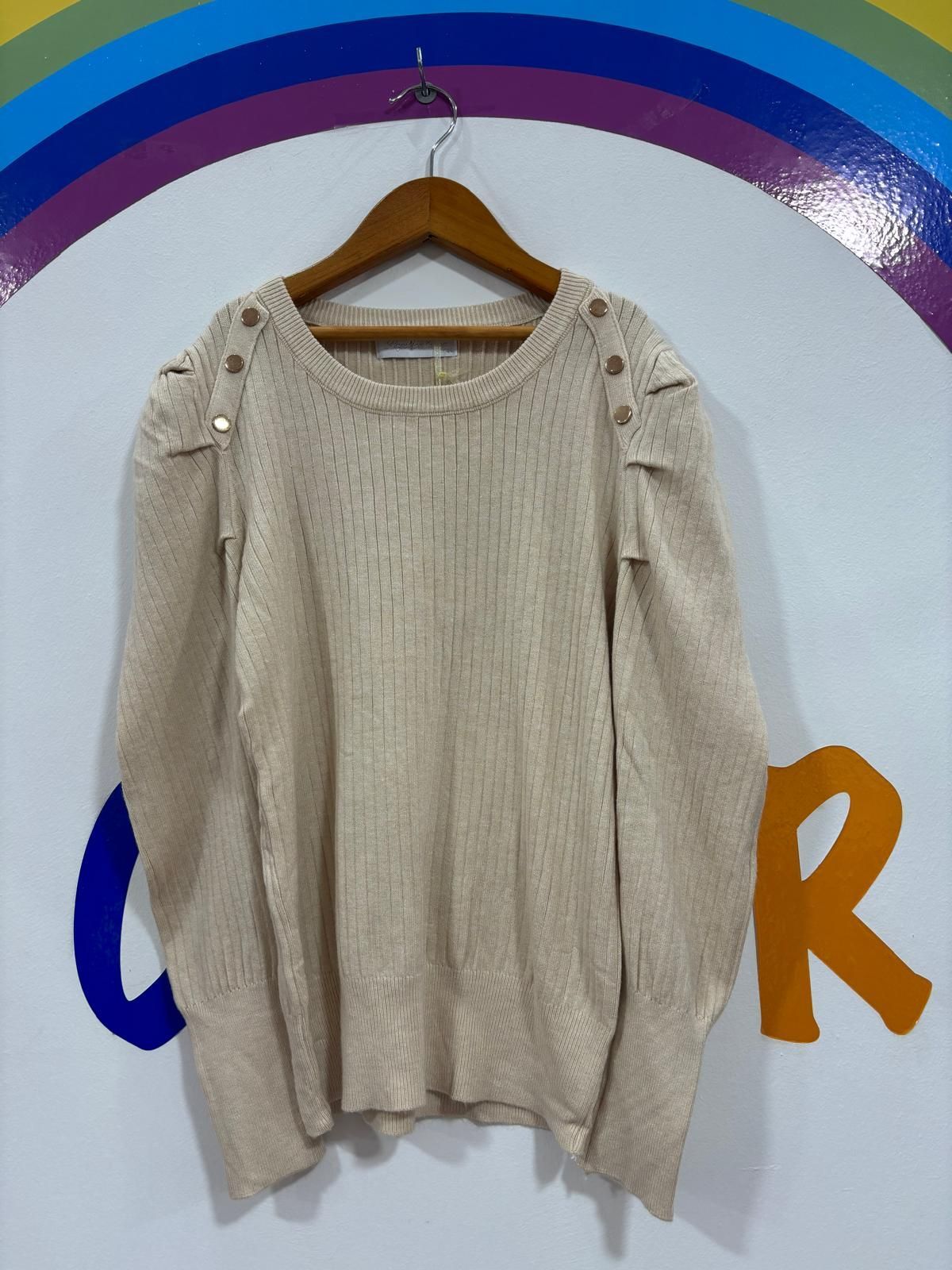 Un suéter blanco cuelga de una percha frente a un arcoíris.