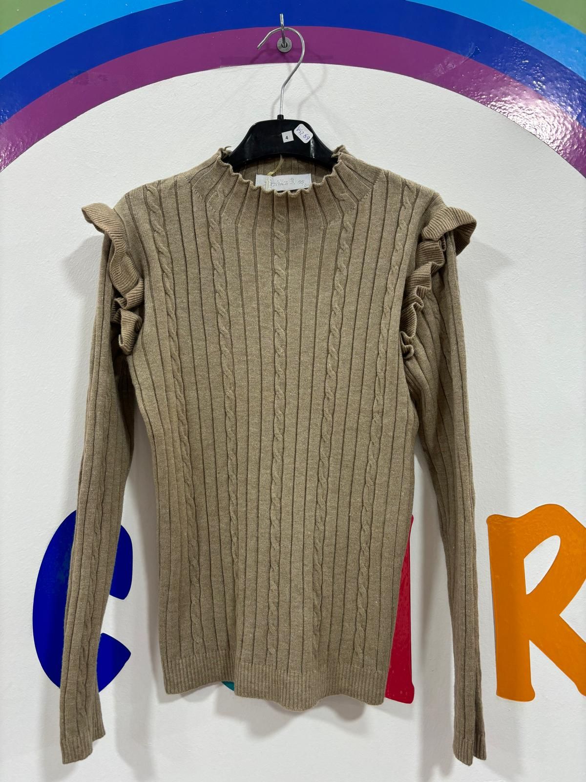 Un suéter con volantes en las mangas está colgado en una percha.