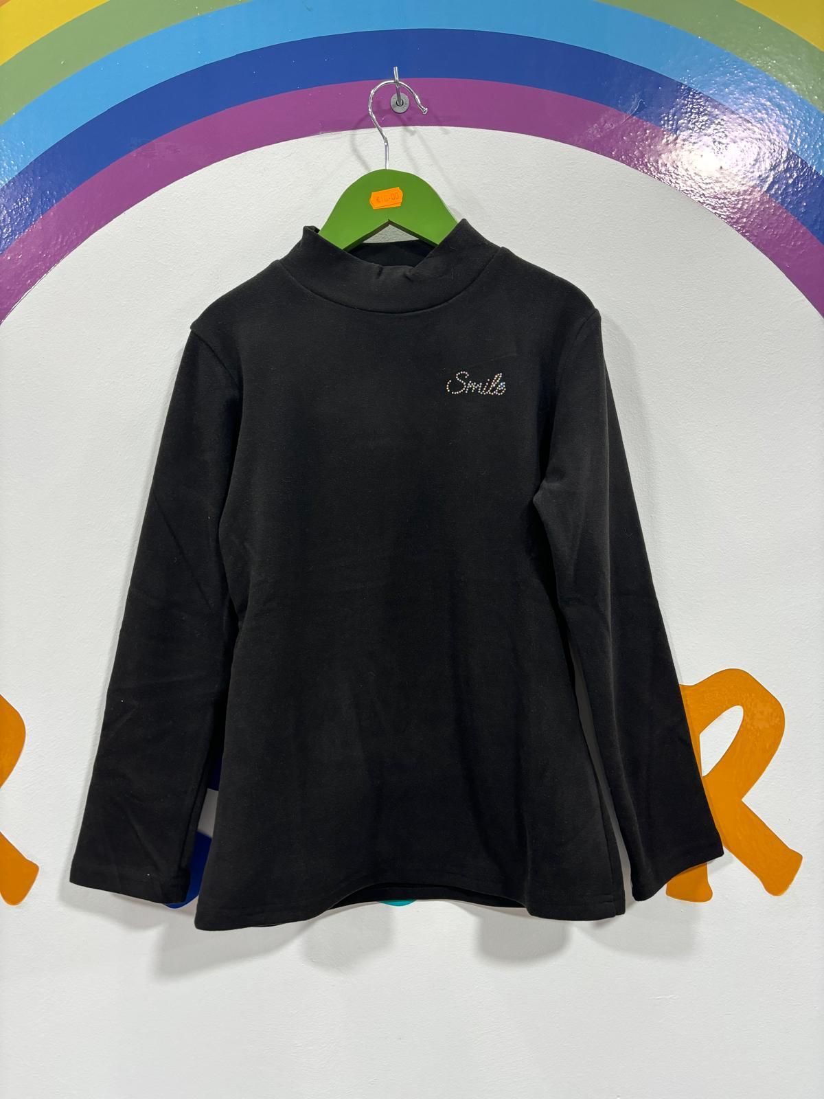 Una camisa negra cuelga de una percha verde frente a un arcoíris.