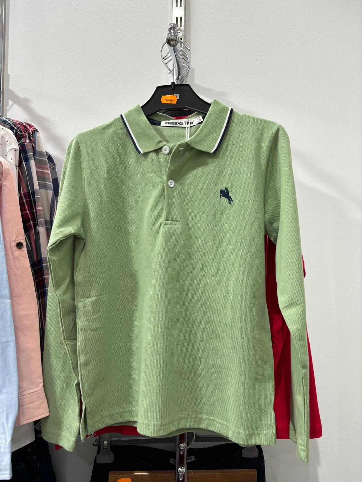 Una camisa polo verde está colgada en un perchero en una tienda.