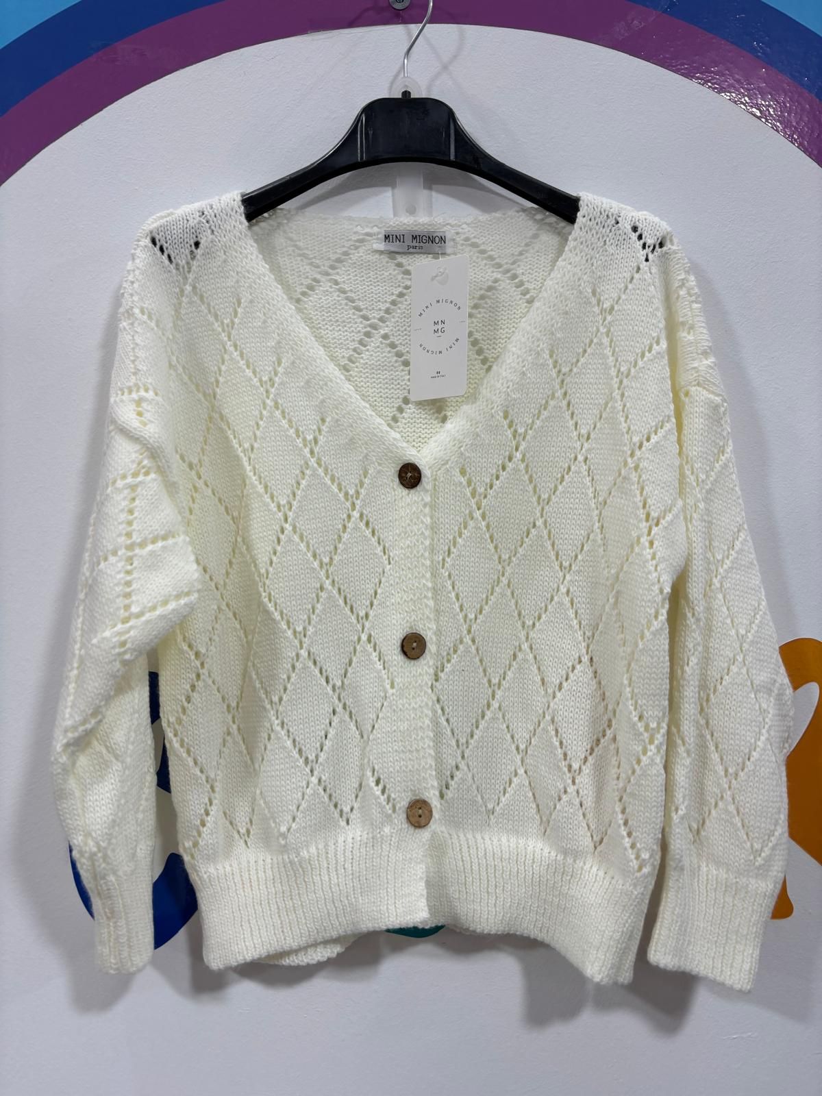 Un suéter blanco con botones está colgado en una percha.
