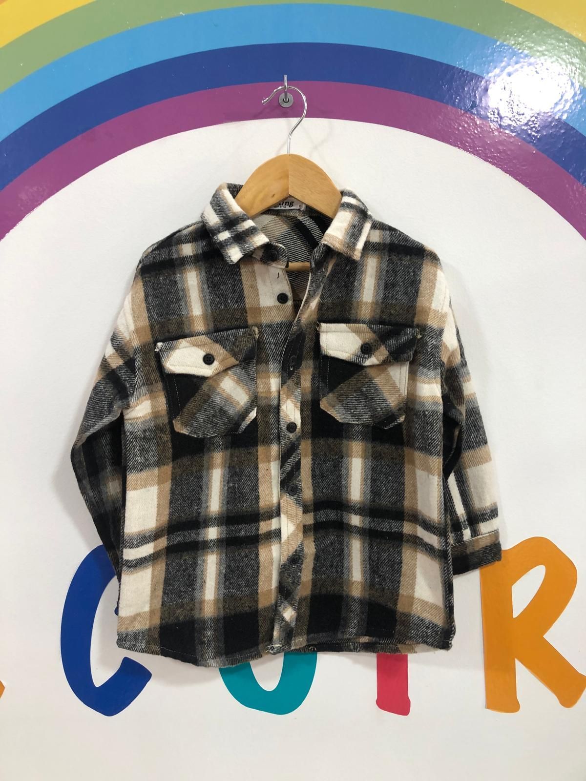 Una camisa a cuadros cuelga de una percha delante de un arcoíris.