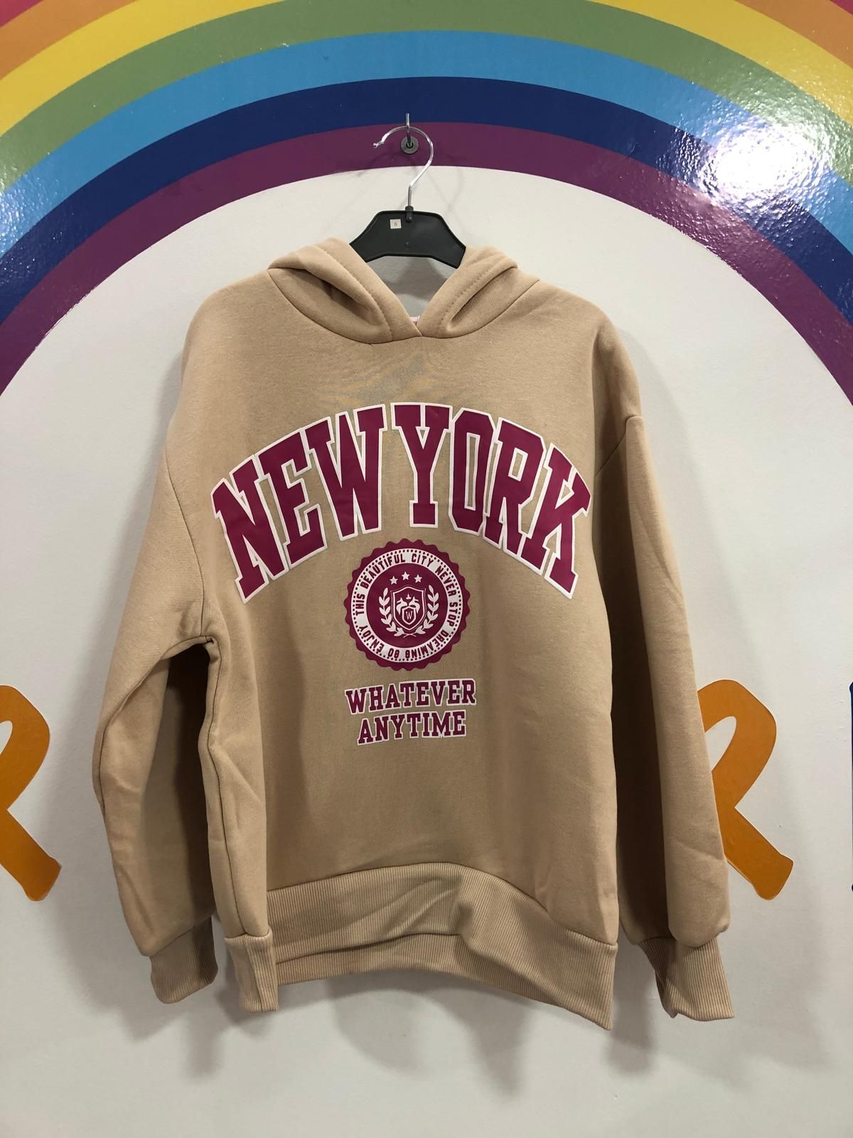 Una sudadera con capucha de Nueva York está colgada en una percha frente a un arcoíris.