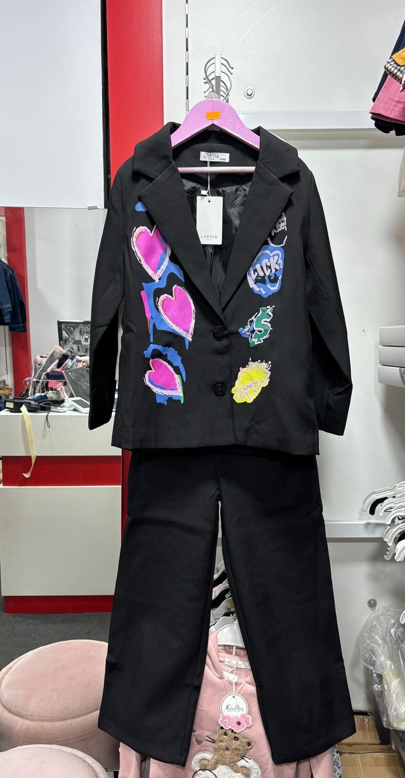 Una chaqueta negra y unos pantalones cuelgan de una percha rosa en una tienda.