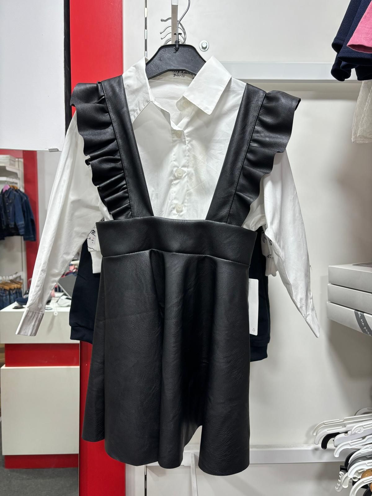 Un vestido negro con tirantes y una camisa blanca cuelgan de una percha en una tienda.
