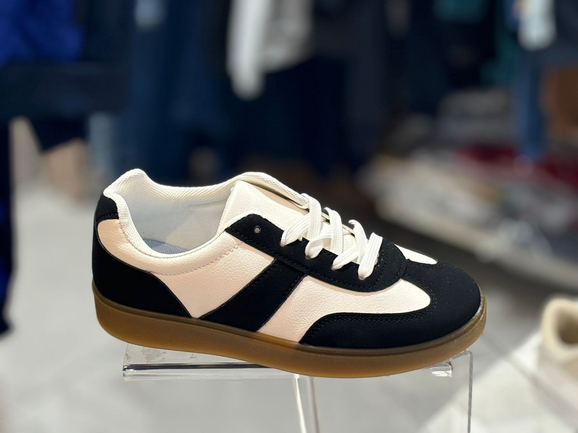 Un par de zapatillas blancas y negras colocadas encima de un expositor transparente.