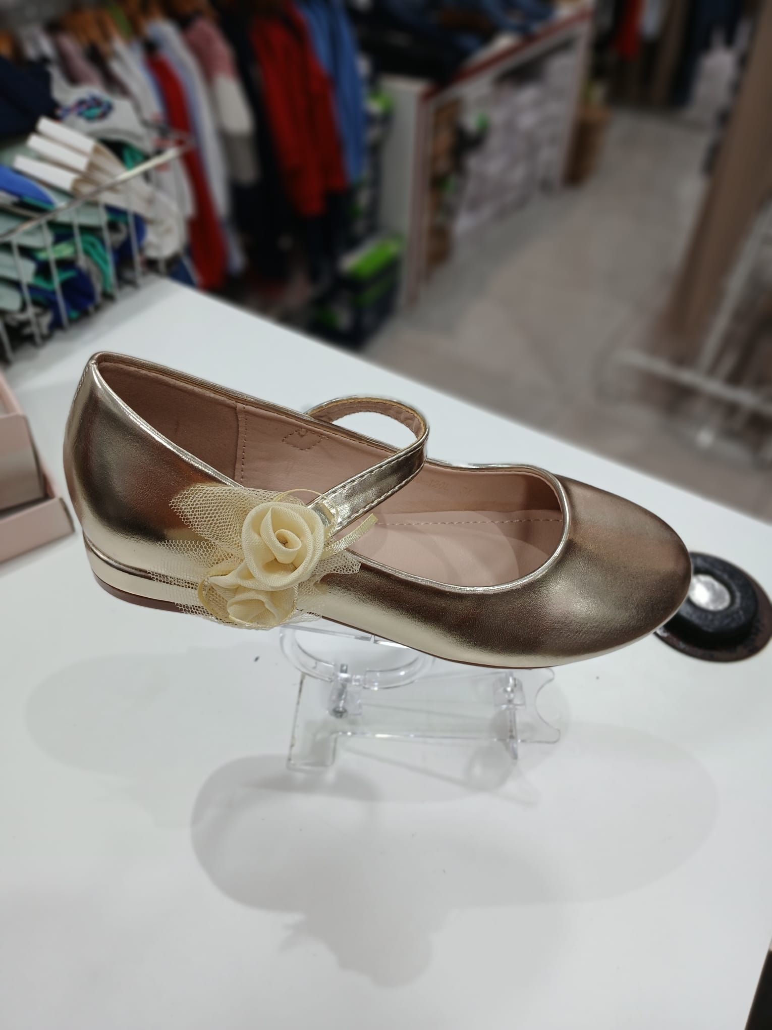 Un par de zapatos dorados con una flor en el costado están sobre una mesa.