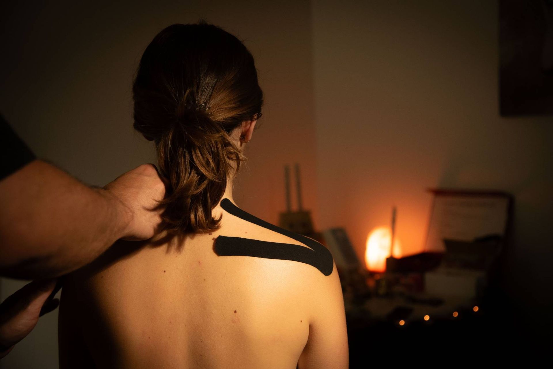 Masaje de espalda en una habitación con poca luz, a la luz cálida de las velas, con una mujer vista de espaldas.