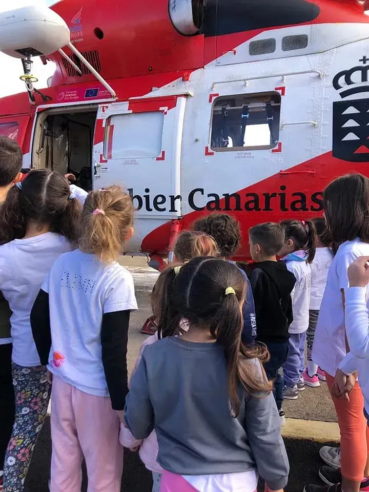 Un grupo de niños está parado frente a un helicóptero rojo y blanco.