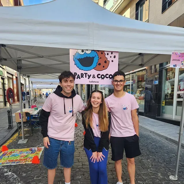 Tres personas paradas bajo una carpa que dice fiesta y coco