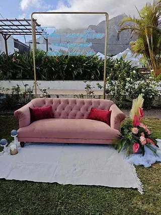 Un sofá rosa está sentado sobre una alfombra blanca en el césped.