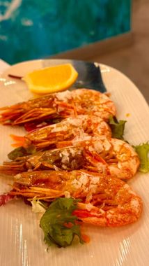 Gambas a la plancha con rodaja de limón y hierbas en un plato blanco.