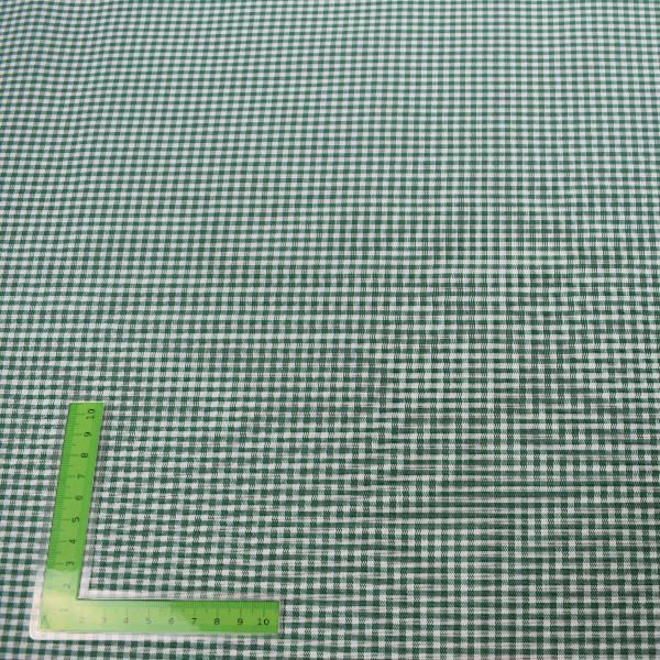 Una regla verde está colocada encima de una tela a cuadros verde y blanca.