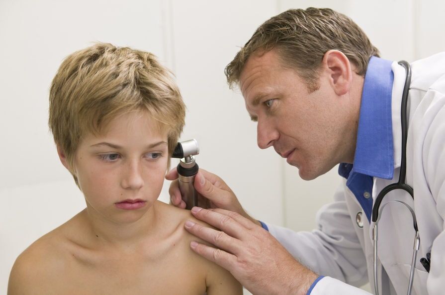 Médico examinando o ouvido de uma criança com um otoscópio em um ambiente clínico.