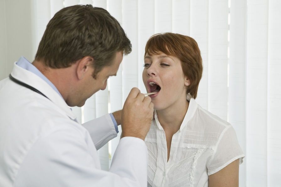 Médico examinando a garganta de um paciente com um abaixador de língua em um consultório médico.
