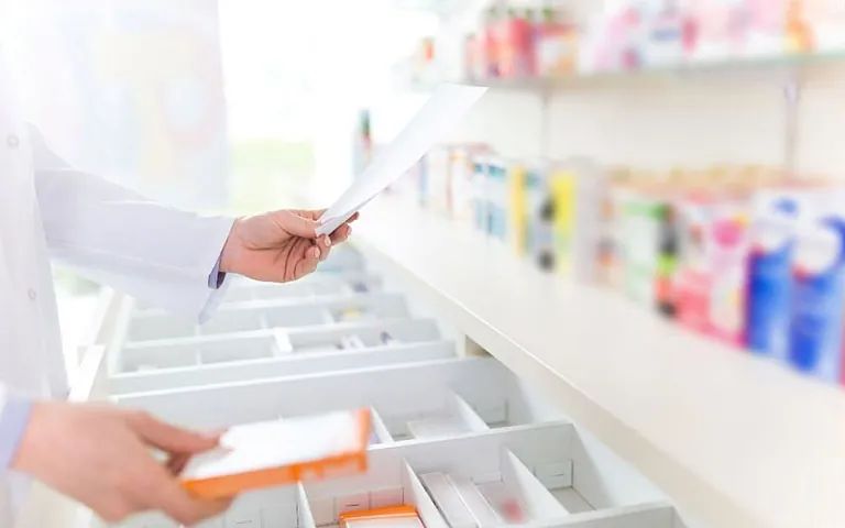 Un farmacéutico está sacando una caja de pastillas de un cajón en una farmacia.