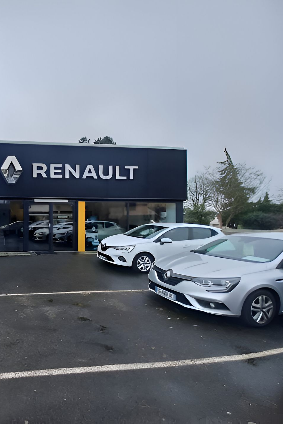Concessionnaire Renault avec des voitures garées à l'extérieur, sous un ciel couvert.