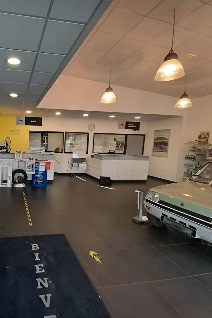 Intérieur d'un showroom automobile avec une voiture verte vintage exposée et un comptoir d'accueil.