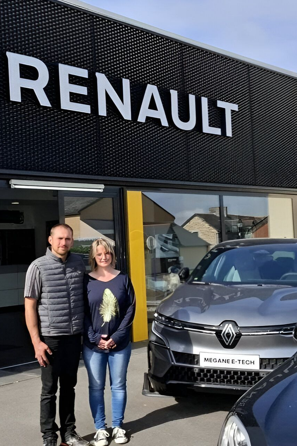 Un couple se tient devant une concession Renault ; une voiture neuve est visible.